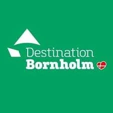 Logo af Destination Bornholm med grøn baggrund, hvid tekst og grafiske former over "Destination" og et rødt hjerte ved "Bornholm".